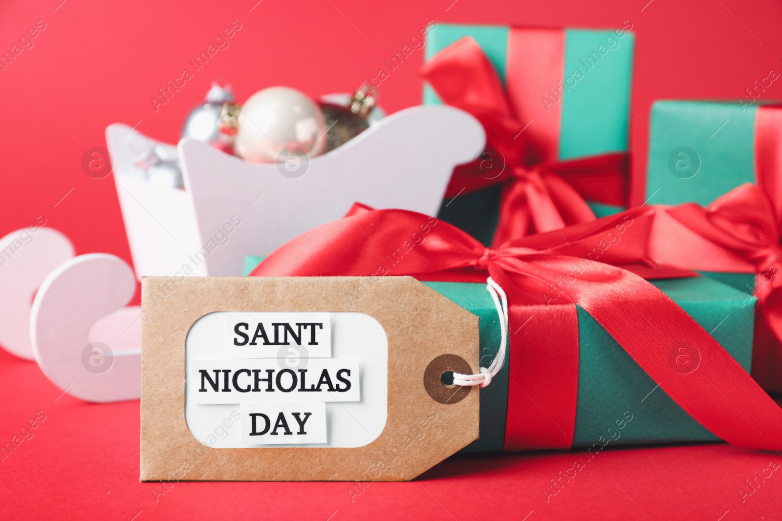 Photo of Gift box and tag with text Saint Nicholas Day on red background, closeup