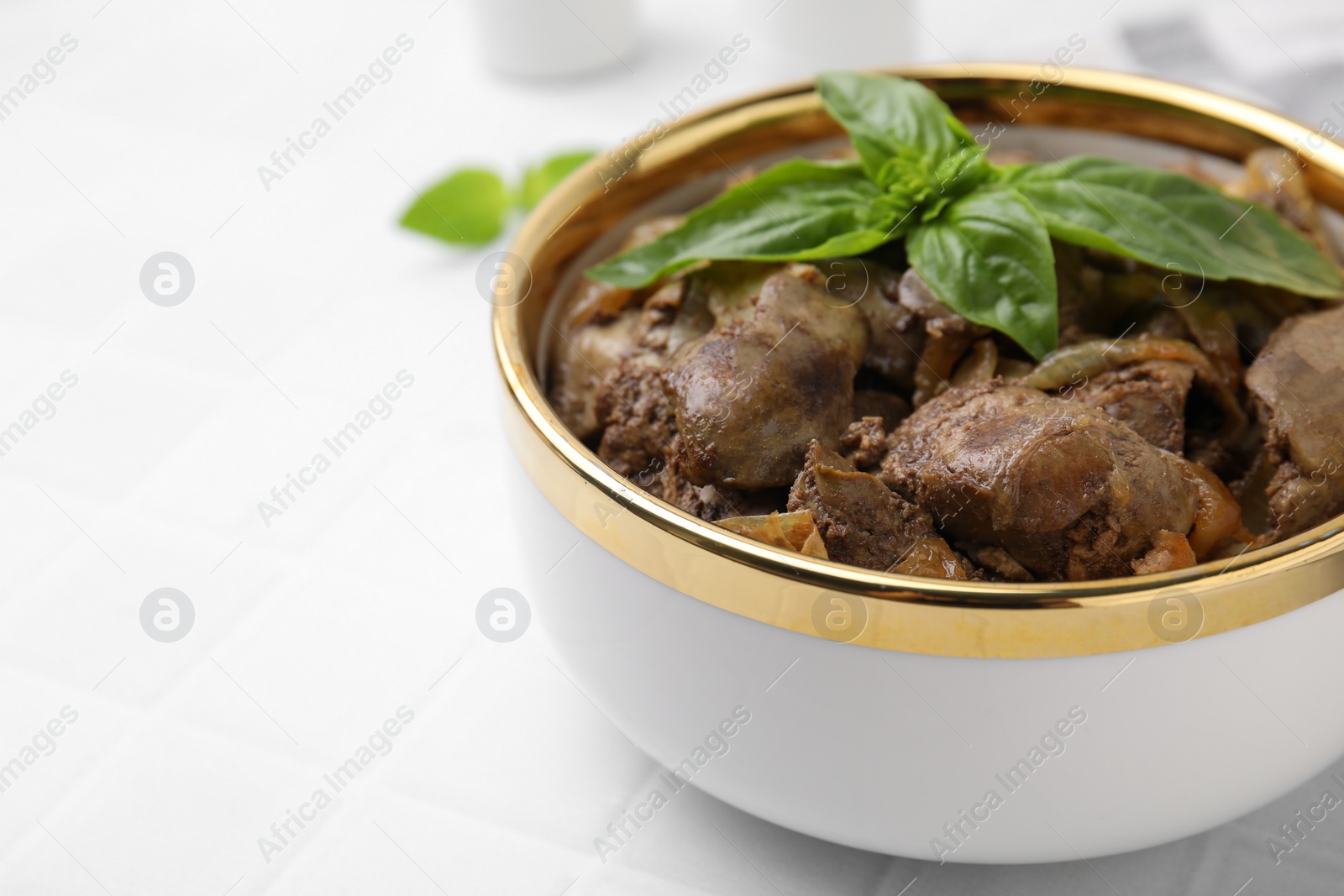 Photo of Delicious fried chicken liver with onion and basil in bowl on white table, closeup. Space for text