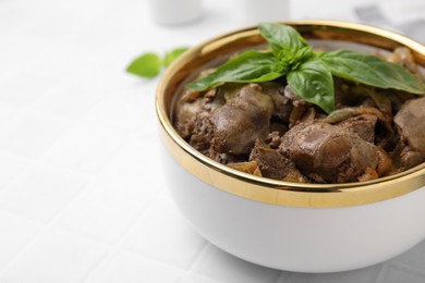 Photo of Delicious fried chicken liver with onion and basil in bowl on white table, closeup. Space for text