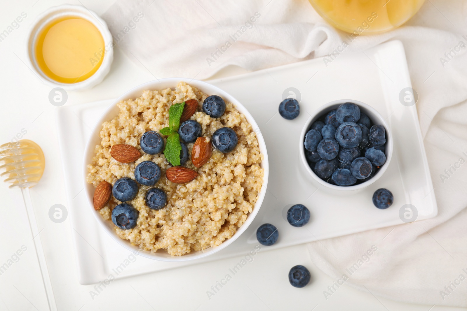 Photo of Bowl of delicious cooked quinoa with almonds and blueberries on white table, flat lay