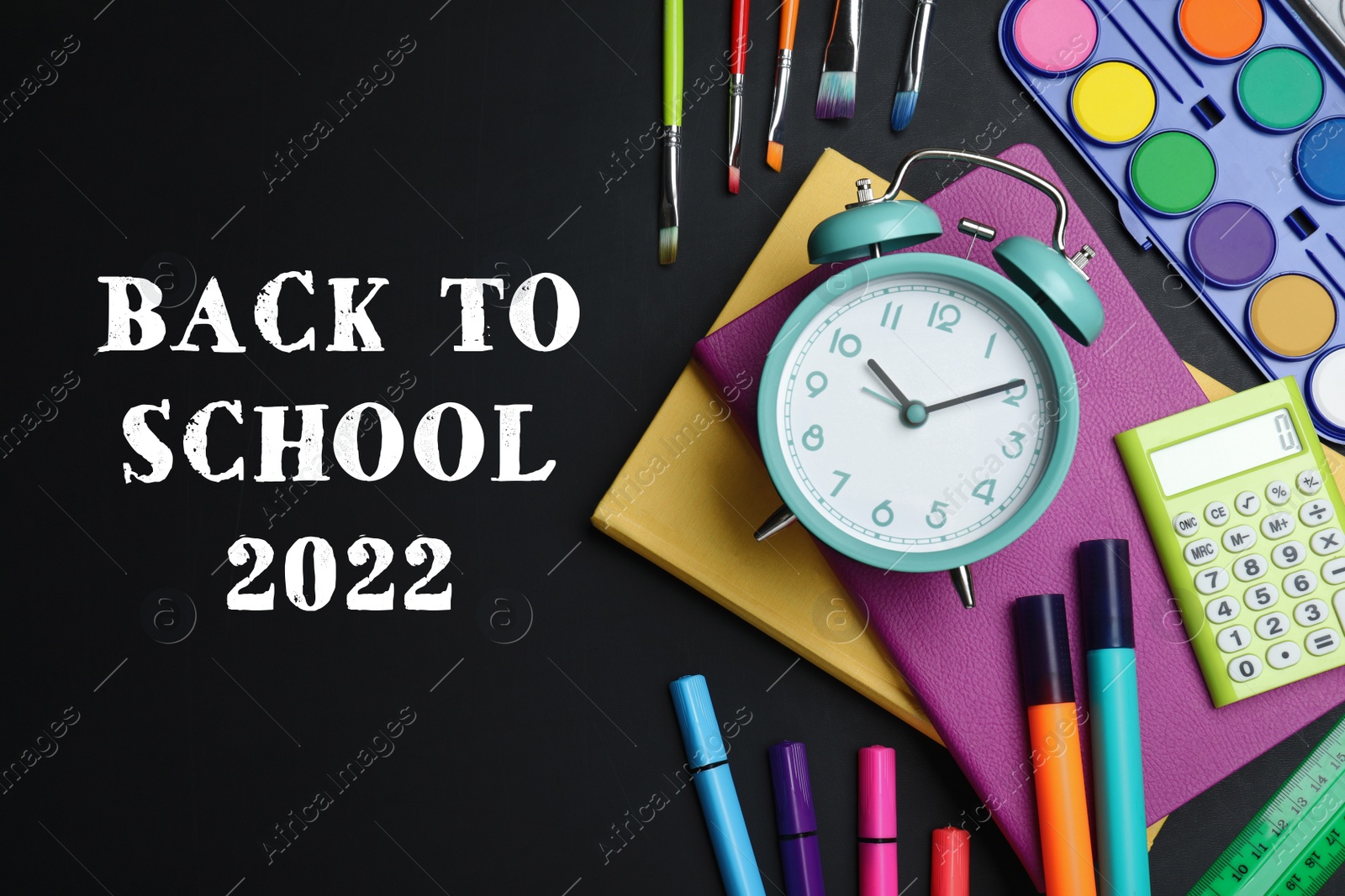 Image of Back to school 2022. Flat lay composition with alarm clock and different stationery on blackboard