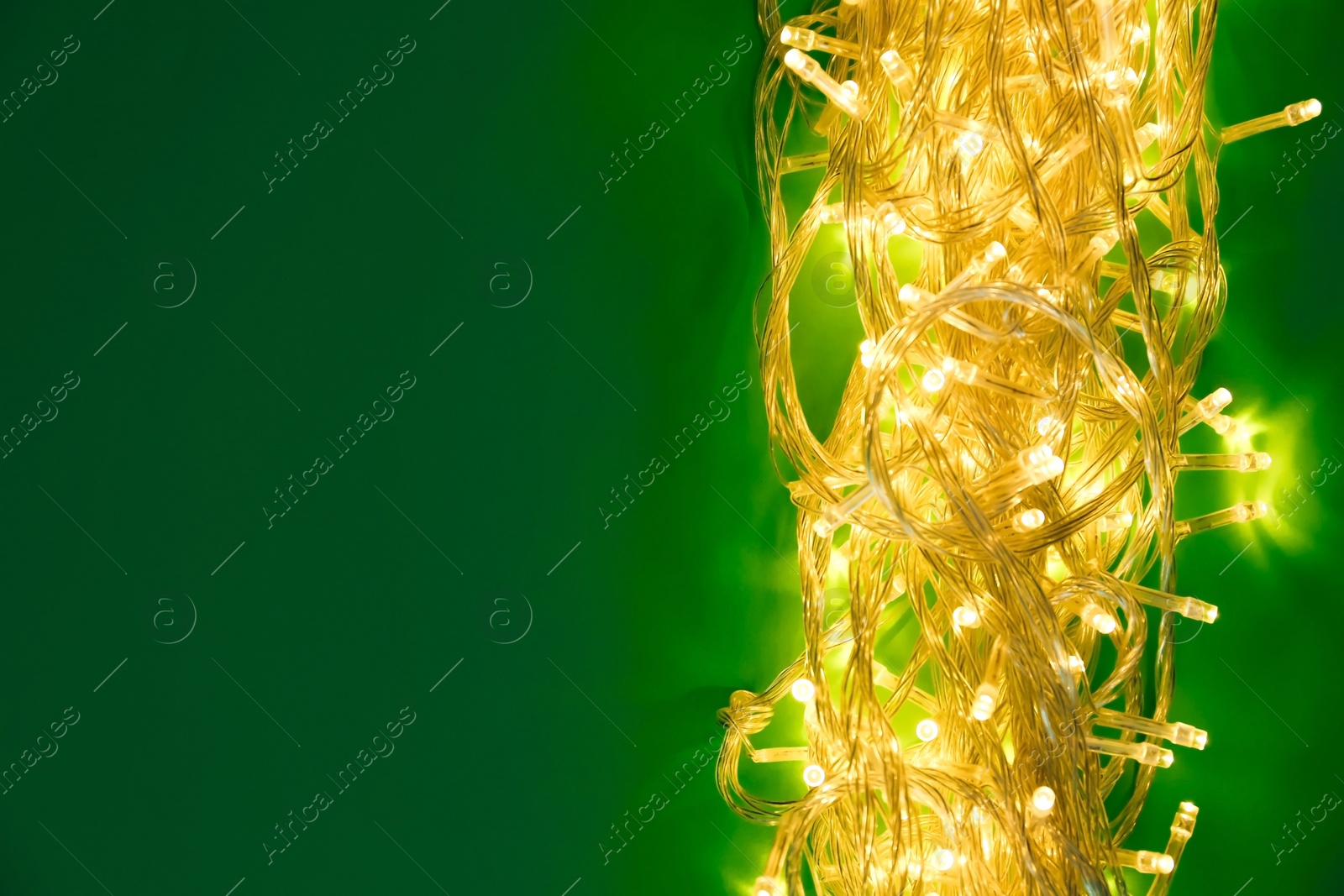 Photo of Glowing Christmas lights on green background, top view. Space for text