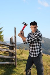 Photo of Handsome man swinging axe in mountains. Professional tool