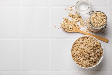 Photo of Delicious pearl barley served on white tiled table, flat lay. Space for text