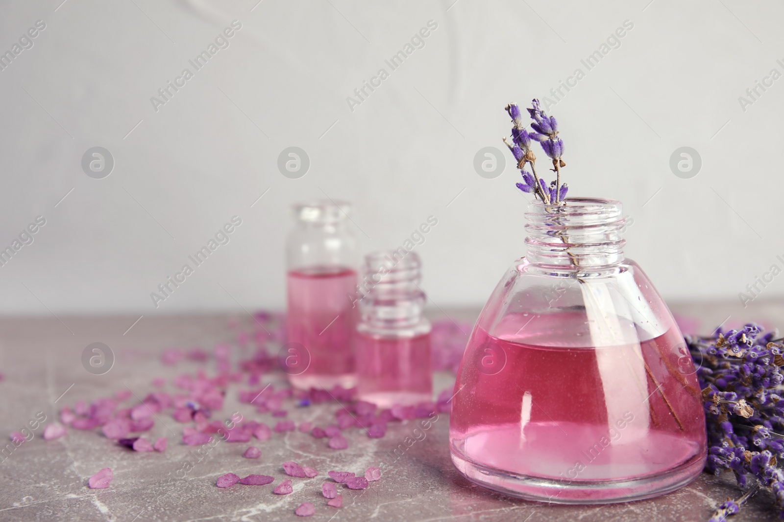 Photo of Bottles with aromatic lavender oil on grey table. Space for text