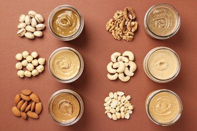 Many tasty nut butters in jars and nuts on brown table, flat lay