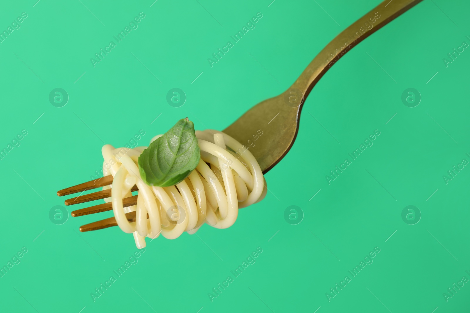 Photo of Fork with tasty pasta and basil on green background, closeup