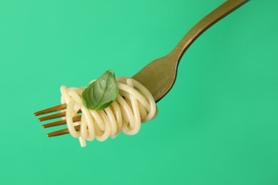 Photo of Fork with tasty pasta and basil on green background, closeup