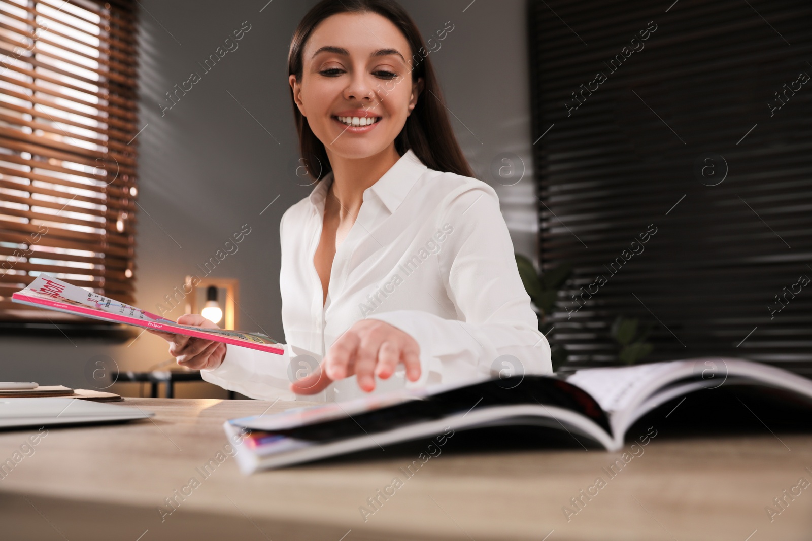 Photo of Happy woman with magazines at workplace in office, low angle view