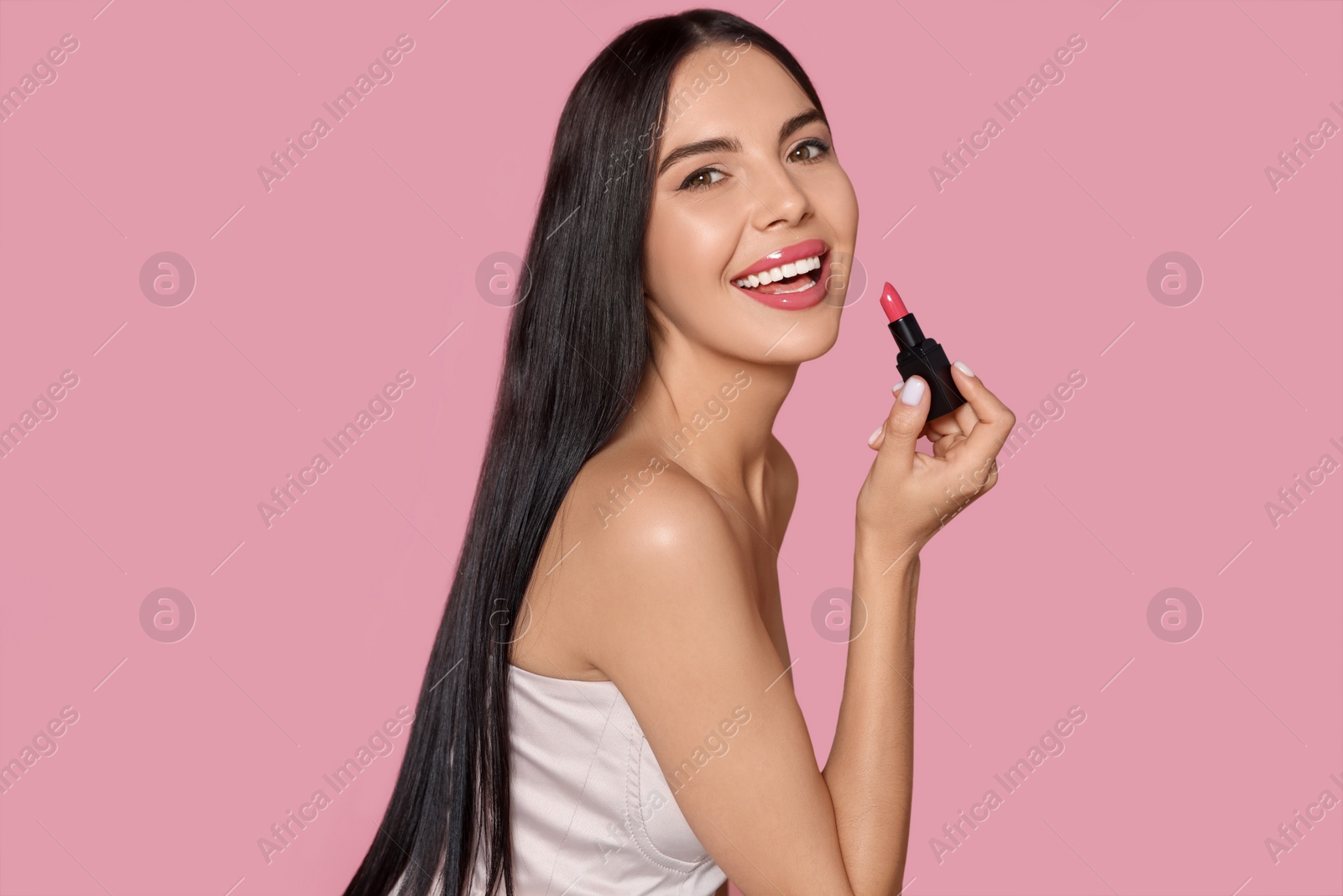 Photo of Young woman with beautiful makeup holding glossy lipstick on pink background