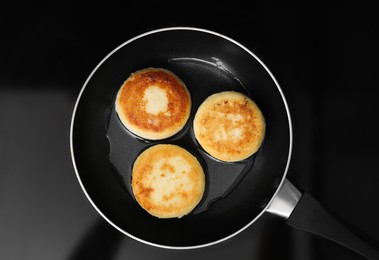 Delicious cottage cheese pancakes in frying pan on cooktop, top view
