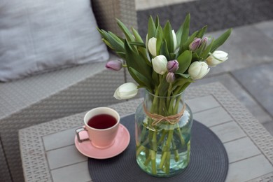 Photo of Beautiful bouquet of colorful tulips and cup with drink on rattan garden table outdoors
