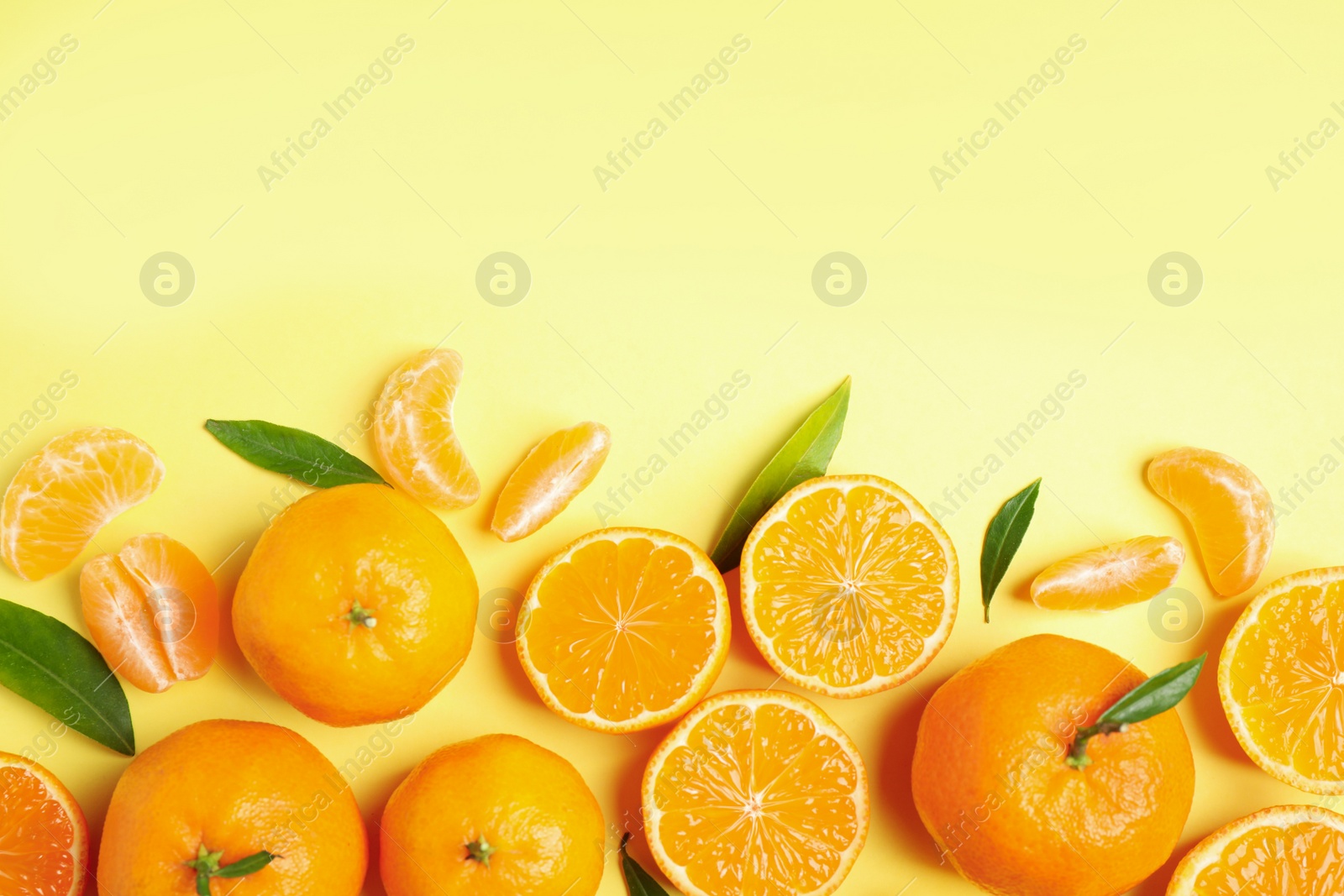 Photo of Flat lay composition with fresh ripe tangerines and leaves on light yellow background, space for text. Citrus fruit