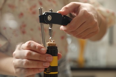 Photo of Woman opening wine bottle with corkscrew on blurred background, closeup