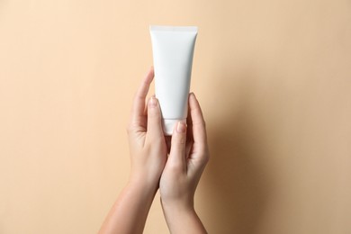 Photo of Woman with tube of hand cream on beige background, closeup