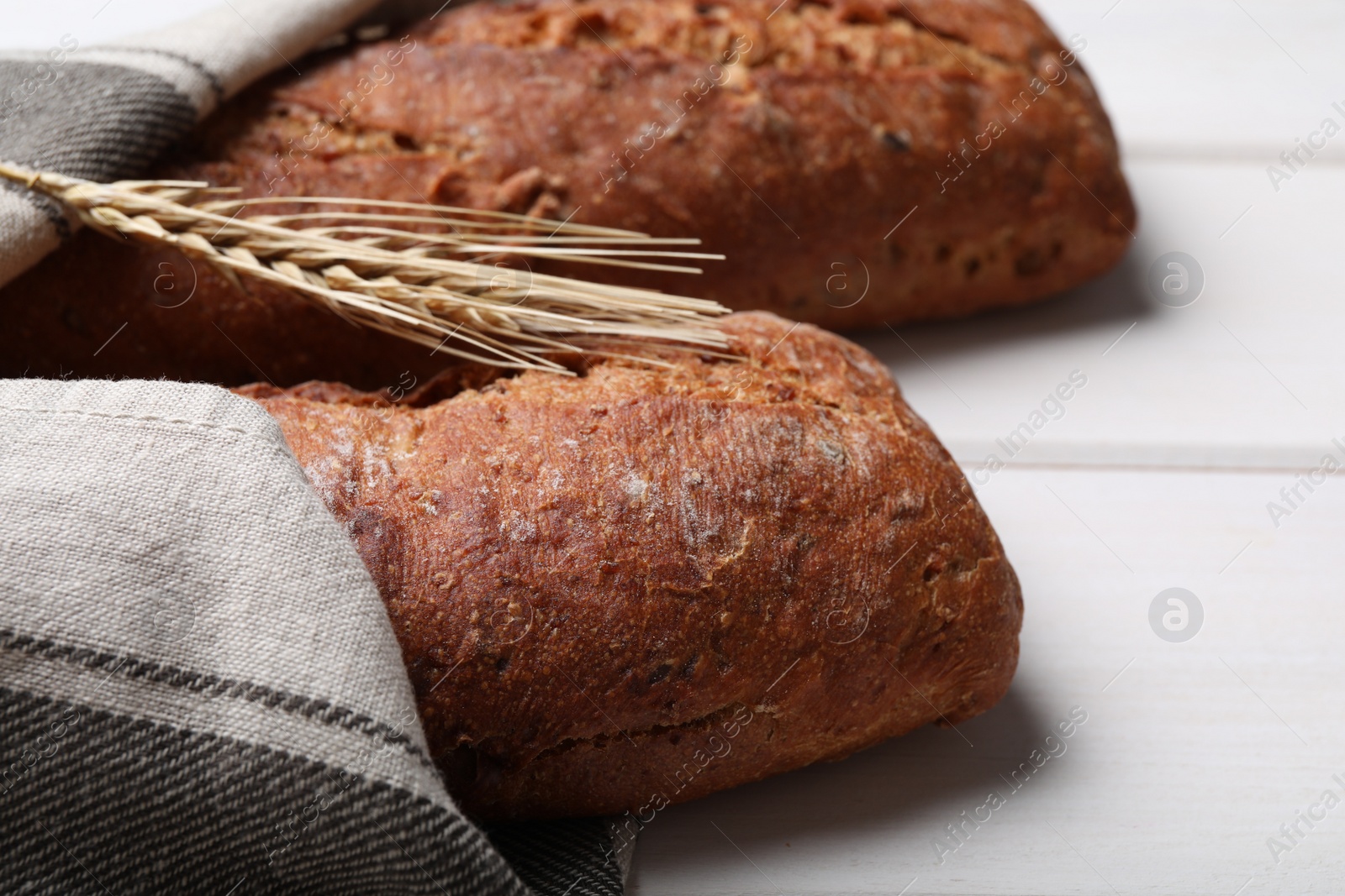 Photo of Tasty rye baguettes and spikelet on white wooden table, closeup