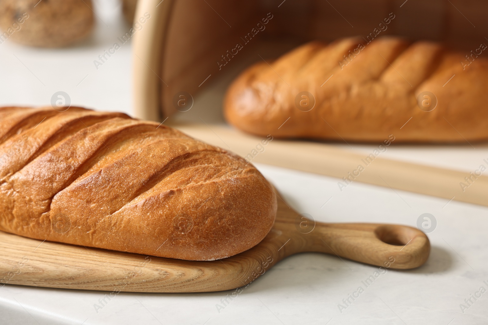 Photo of Wooden bread basket with freshly baked loaves on white marble table in kitchen, closeup