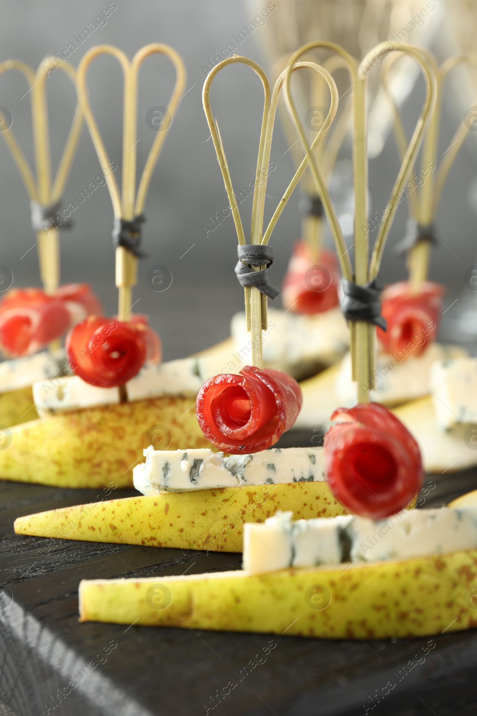 Photo of Tasty canapes with pears, blue cheese and prosciutto on grey table, closeup