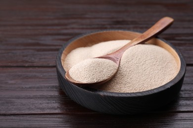 Photo of Bowl and spoon with active dry yeast on wooden table, closeup. Space for text