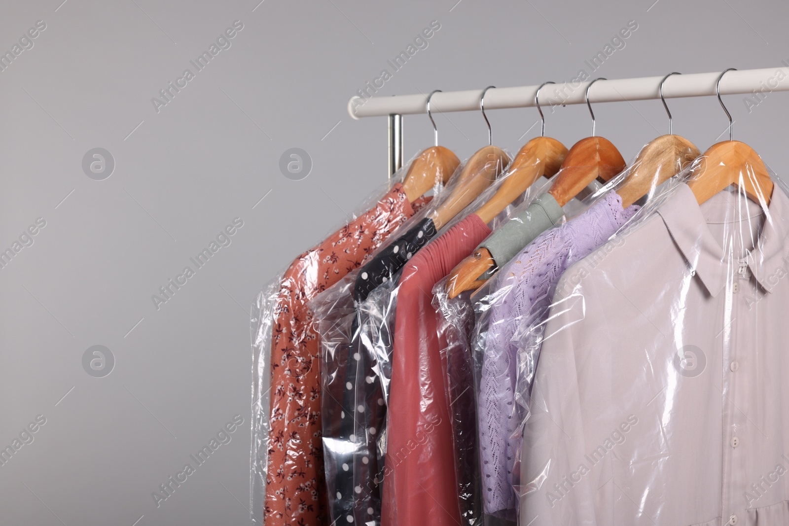 Photo of Dry-cleaning service. Many different clothes in plastic bags hanging on rack against grey background, space for text