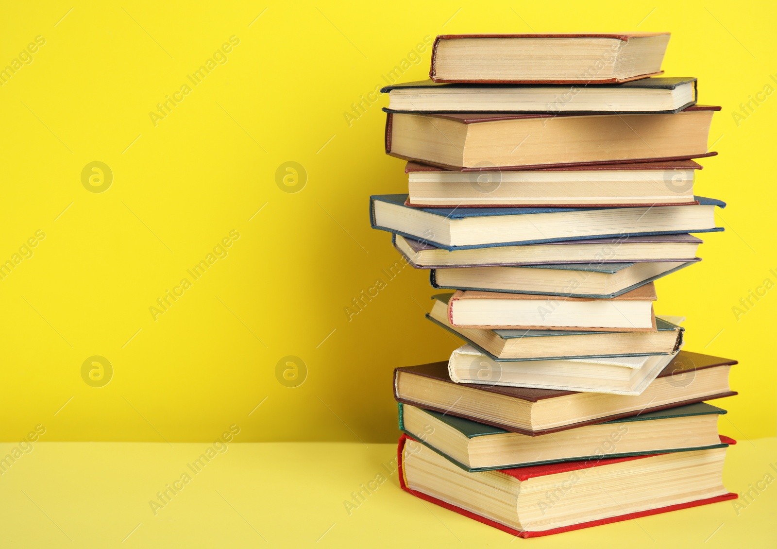 Photo of Stack of hardcover books on yellow background. Space for text