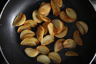 Photo of Frying pan with fried garlic cloves, top view