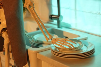 Photo of Human skeleton washing dishes in kitchen sink at night, closeup