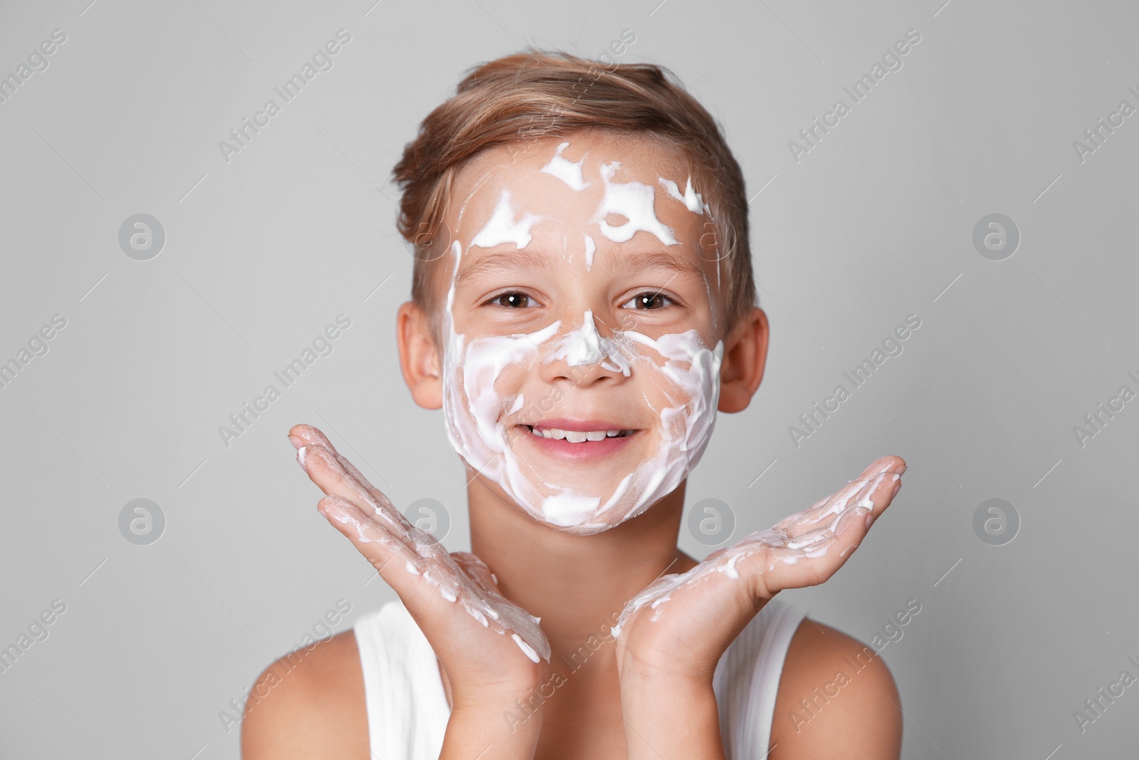Photo of Cute little boy with soap foam on face against gray background