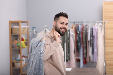 Photo of Dry-cleaning service. Happy man holding hanger with jacket in plastic bag indoors