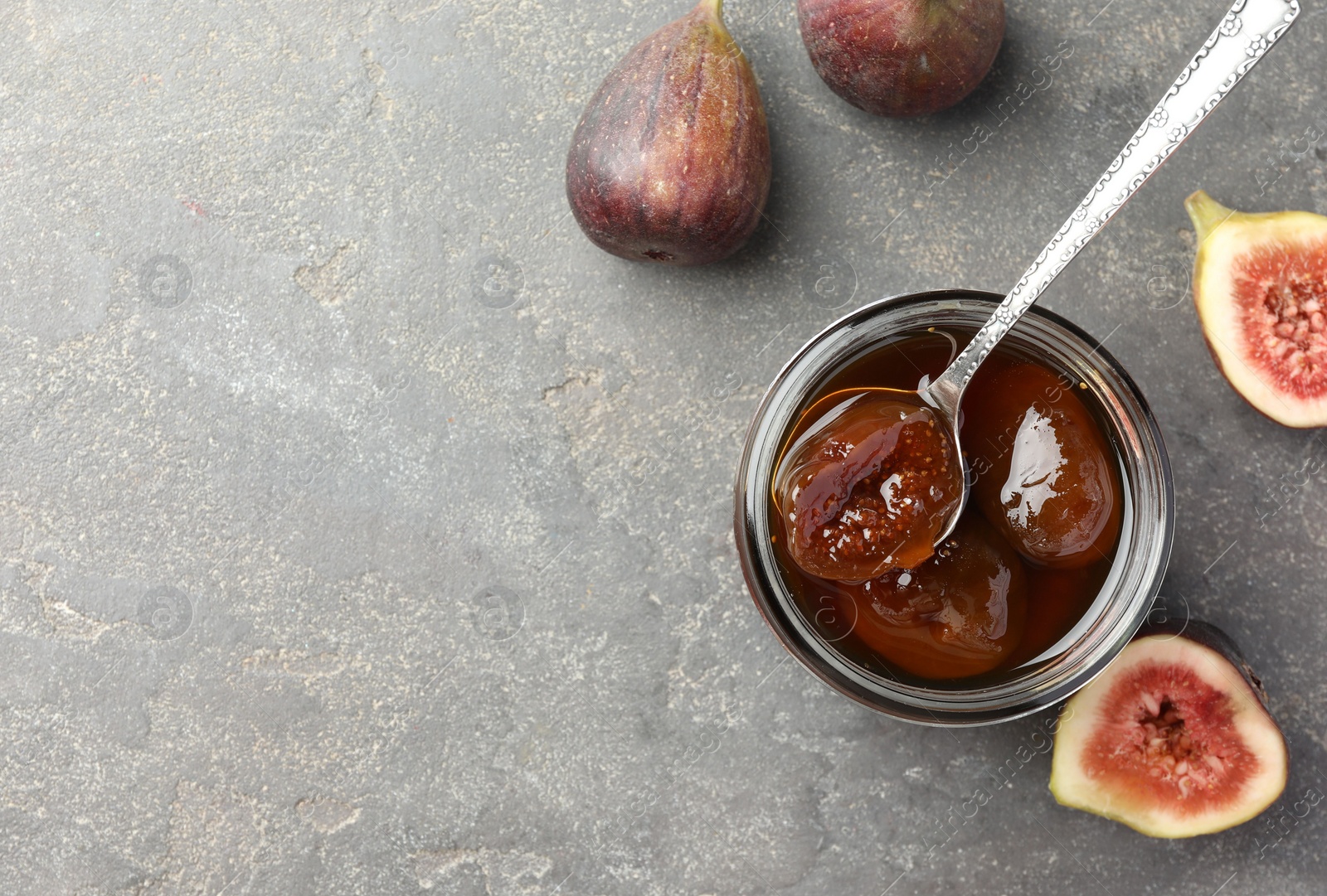 Photo of Jar of tasty sweet jam and fresh figs on grey table, flat lay. Space for text