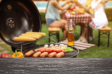Image of Empty black wooden table and blurred view of tasty food on modern barbecue grill outdoors