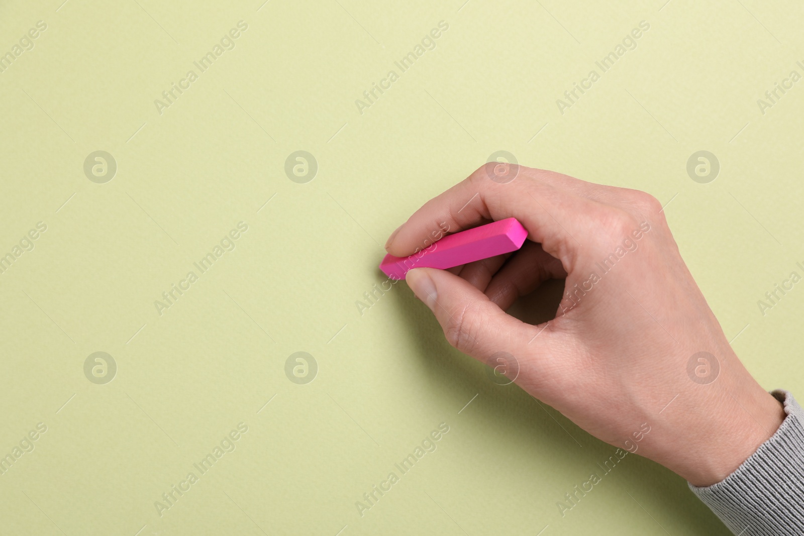 Photo of Woman drawing on light green paper with pastel, top view. Space for text