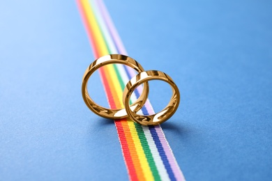 Photo of Wedding rings and rainbow ribbon on color background. Gay symbol