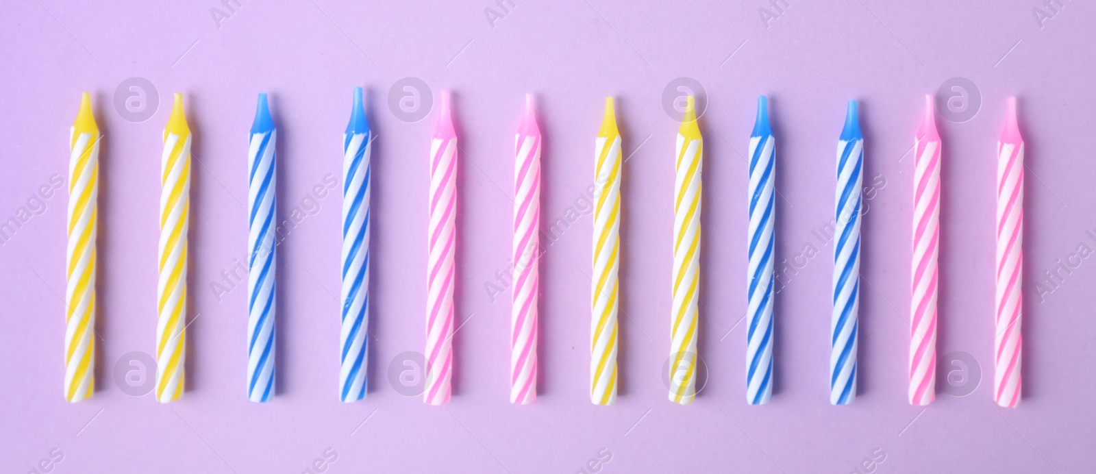 Photo of Colorful striped birthday candles on lilac background, flat lay