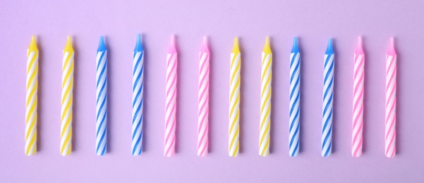 Photo of Colorful striped birthday candles on lilac background, flat lay