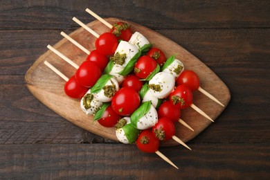 Photo of Caprese skewers with tomatoes, mozzarella balls, basil and pesto sauce on wooden table, top view