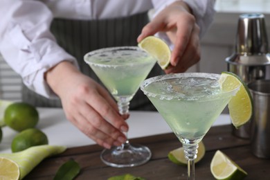 Photo of Bartender putting piece of lime onto glass with delicious Margarita cocktail at wooden table, closeup