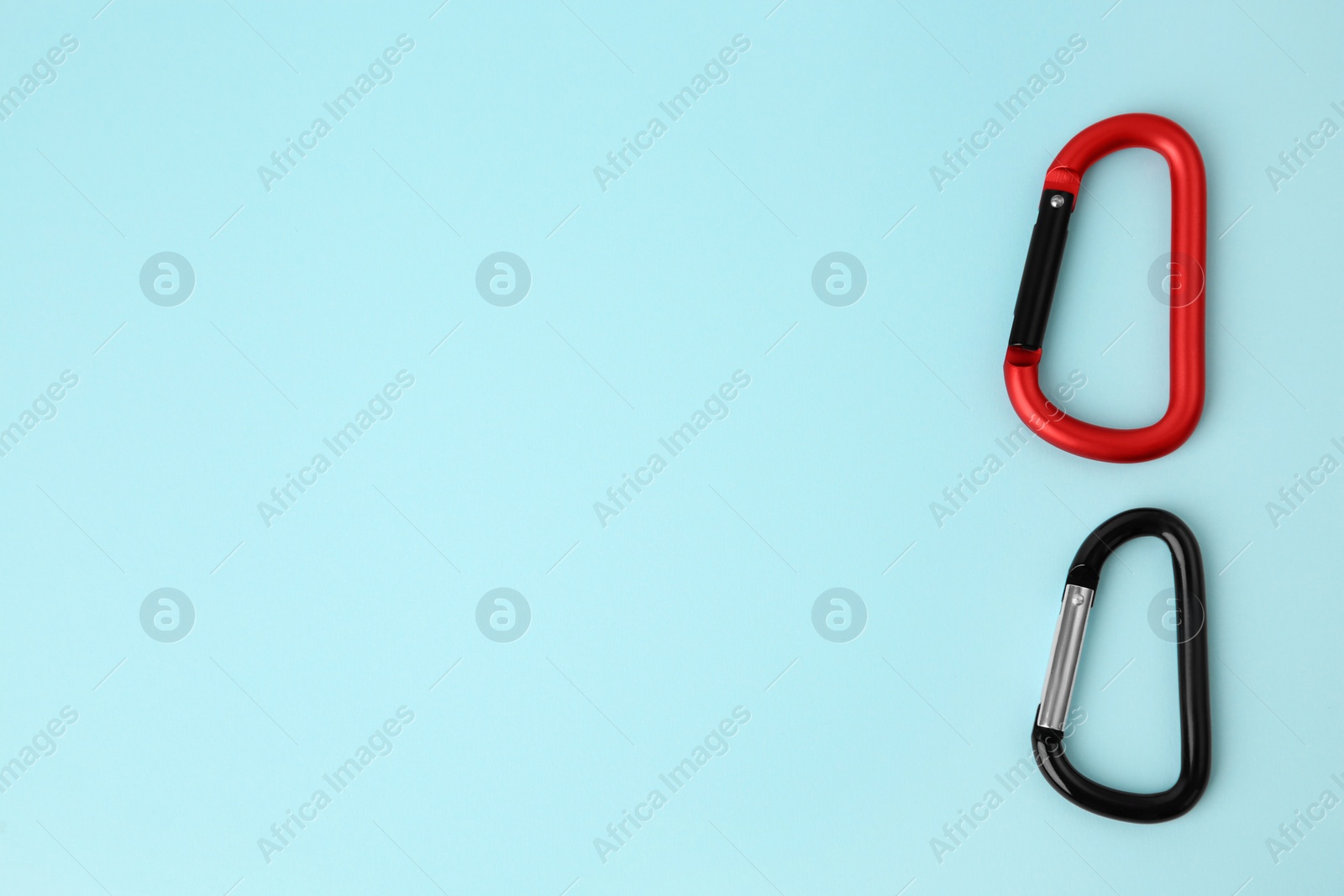 Photo of Two metal carabiners on light blue background, flat lay. Space for text