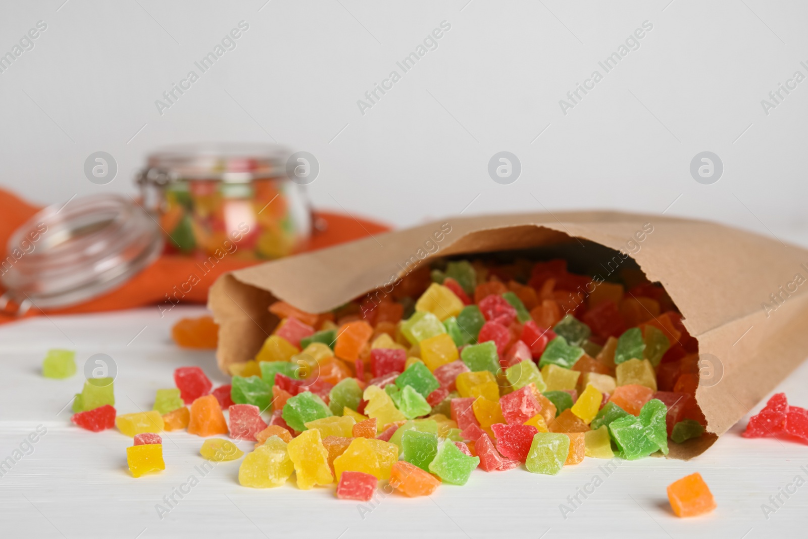 Photo of Overturned paper bag with mix of delicious candied fruits on white table, space for text