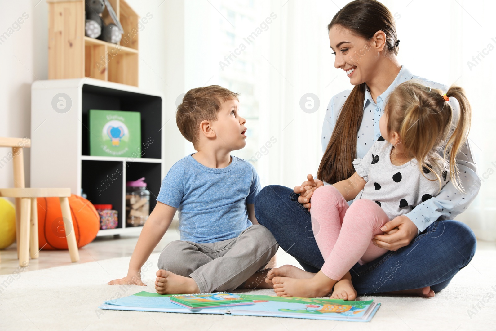 Photo of Kindergarten teacher reading book to children indoors. Learning and playing