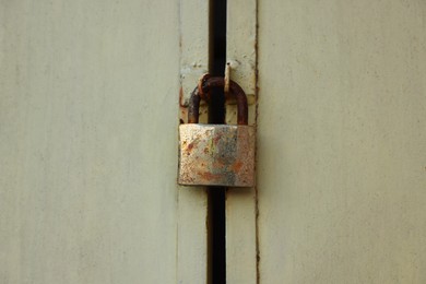 Closed rusty metal padlock on beige gates, closeup