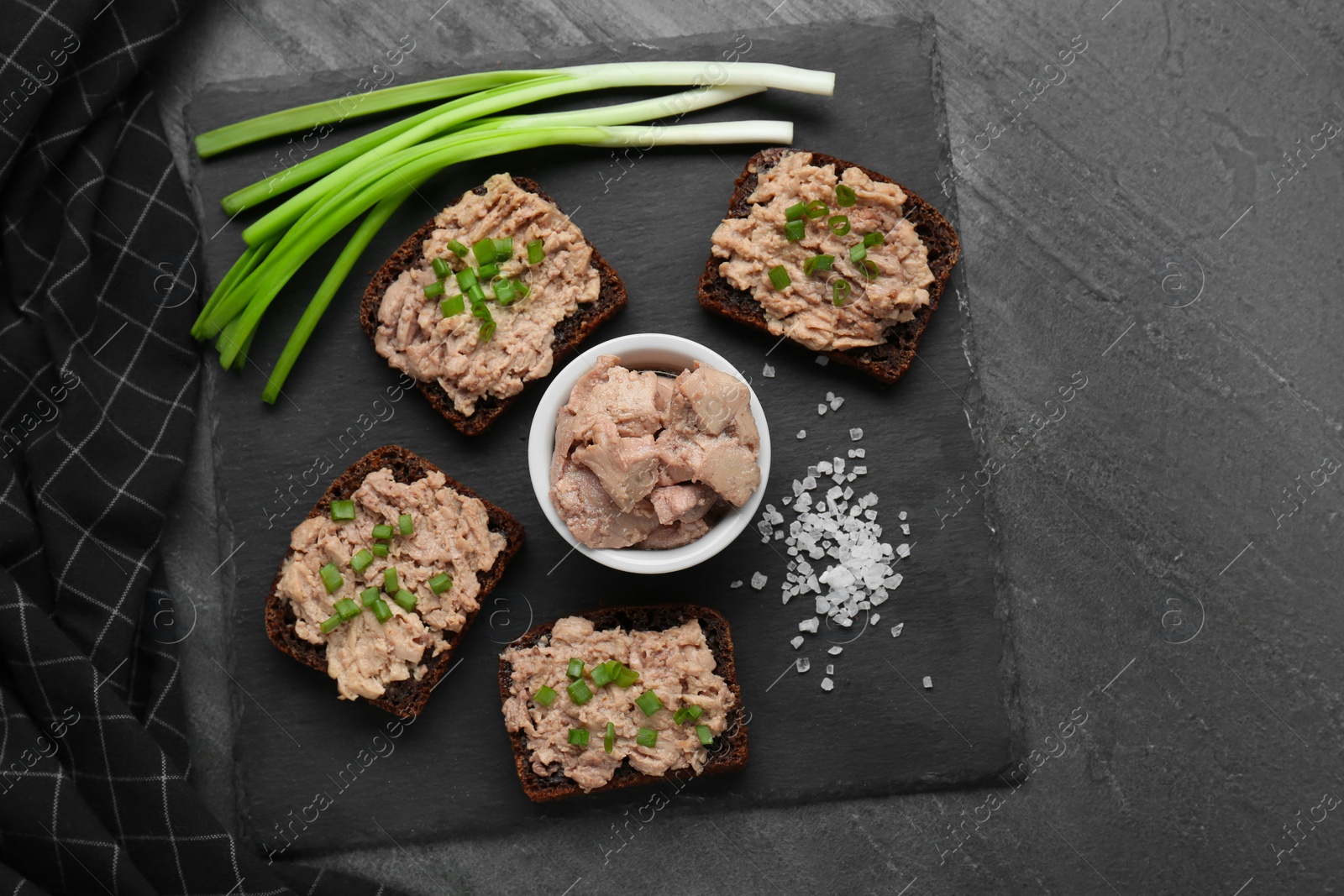 Photo of Tasty sandwiches with cod liver, salt and green onion on grey table, top view