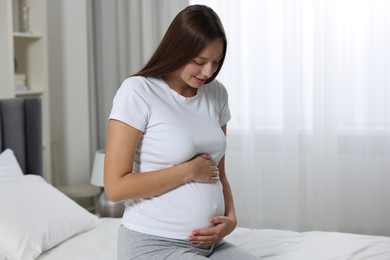 Beautiful pregnant woman with long hair in bedroom, space for text