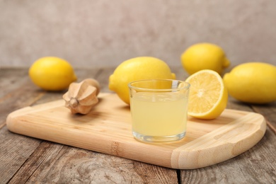 Photo of Wooden board with glass of freshly squeezed lemon juice and reamer on table