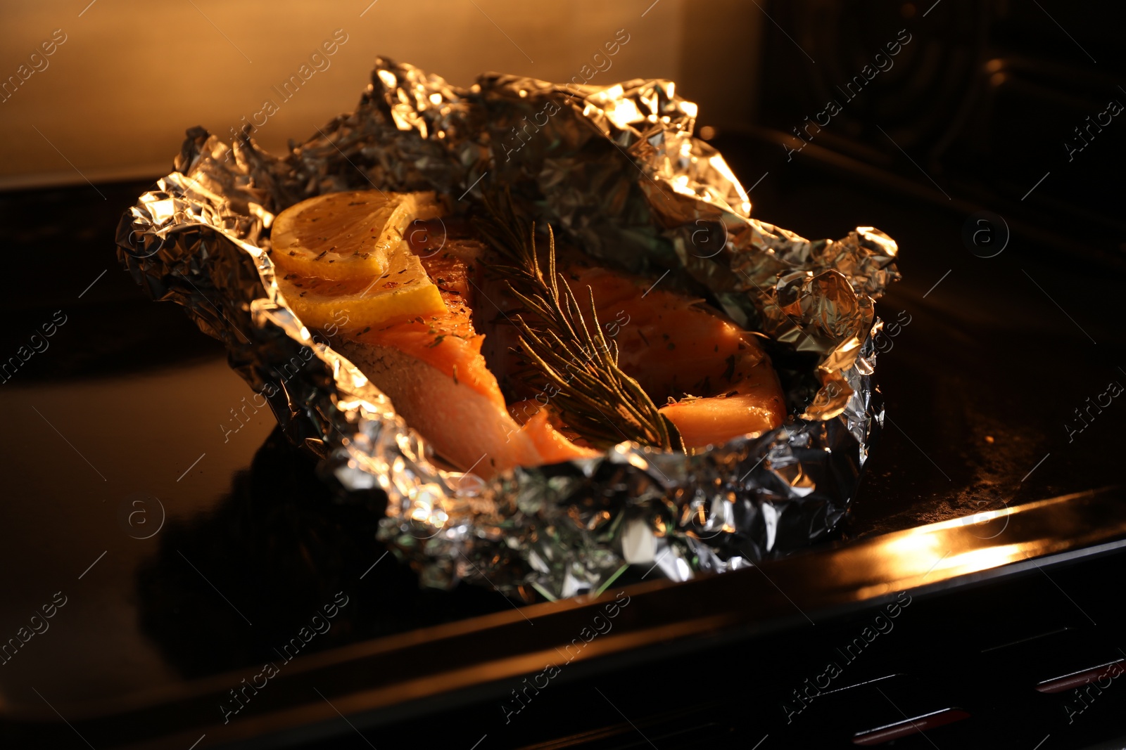 Photo of Foil with fish in oven, closeup. Baking salmon