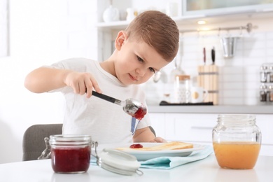 Photo of Cute little boy spreading sweet jam onto toast at table
