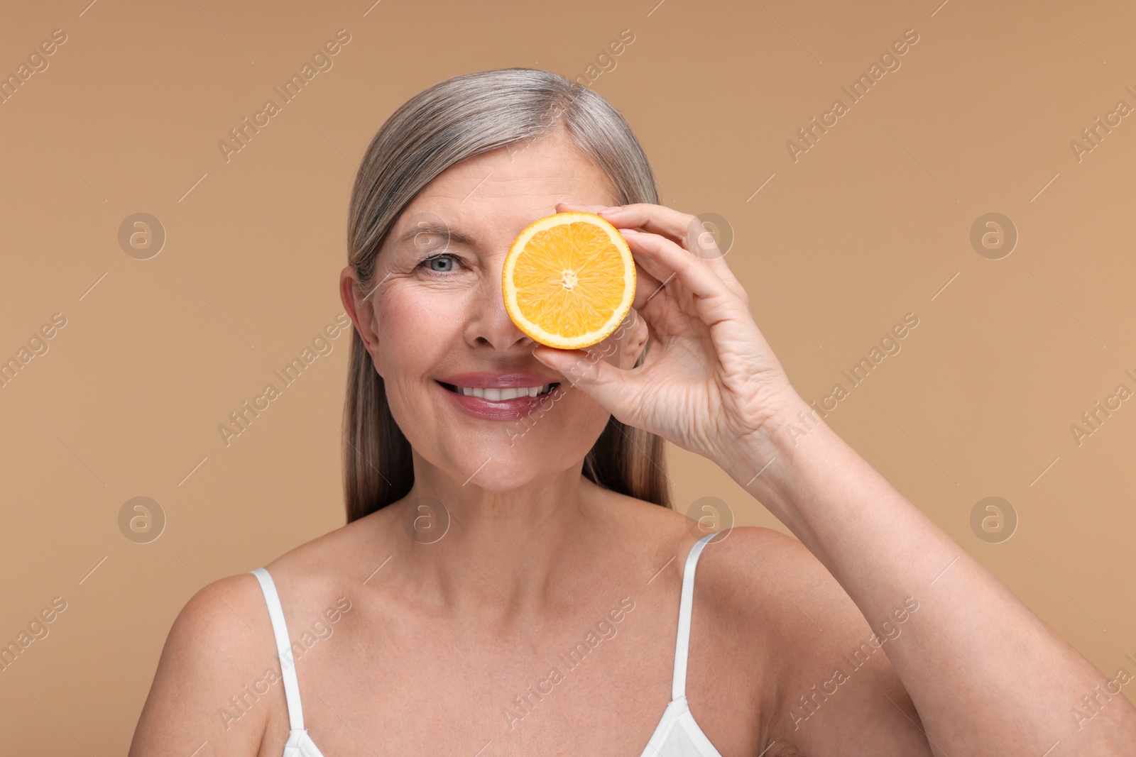 Photo of Beautiful woman with half of orange rich in vitamin C on beige background