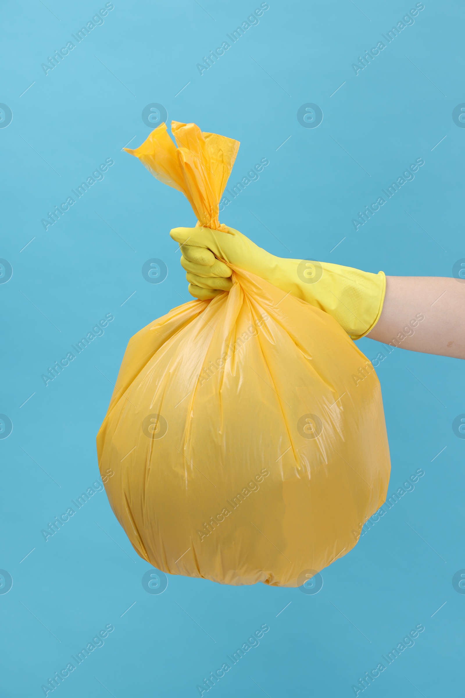 Photo of Woman holding plastic bag full of garbage on light blue background, closeup