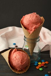 Photo of Delicious pink ice cream in wafer cones and candies  on black wooden table