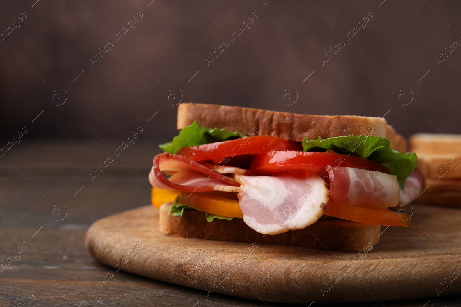 Photo of Tasty sandwich with bacon and tomato on wooden table, closeup